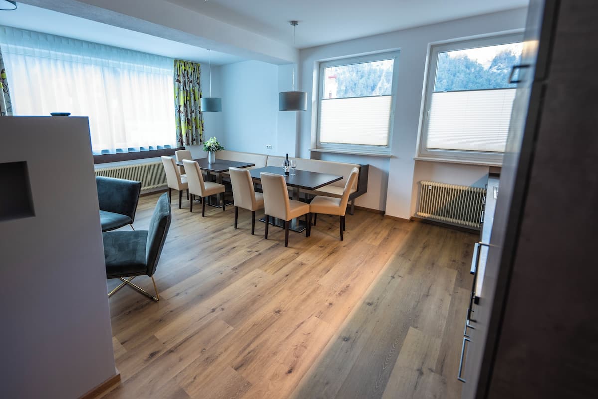 Un espace repas moderne avec une table et des chaises en bois, de grandes fenêtres équipées de stores et un radiateur.