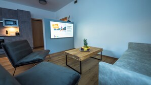 A modern living room with a wooden coffee table, two grey sofas, and a kitchen area with a microwave and cabinets. - Apart Inntalerhof (Toesens)