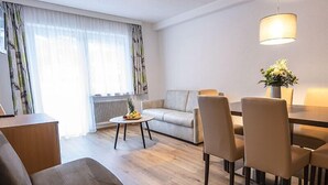 A modern living room with a sofa, dining table, chairs, and a coffee table. - Apart Inntalerhof (Toesens)