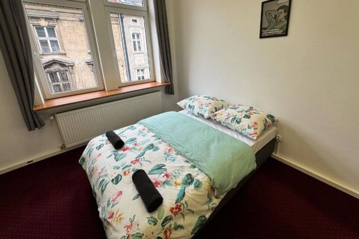 A single bed with floral bedding, a window with curtains, and a radiator below.