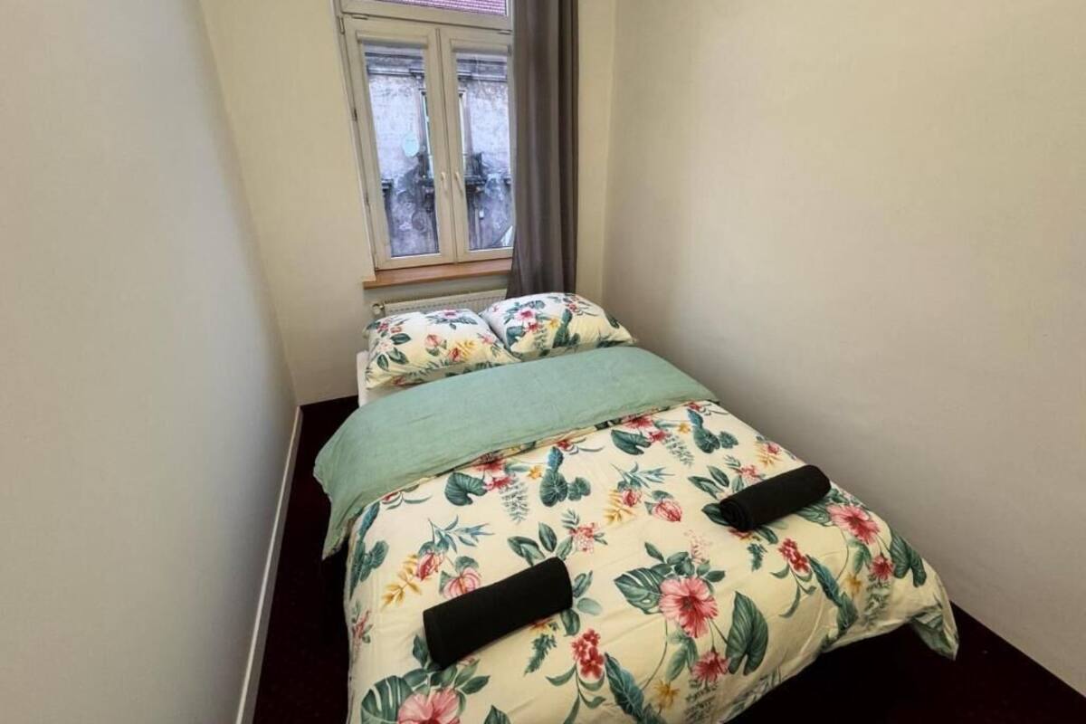 A small bedroom with a bed, floral bedding, a window, and a view of the outside.