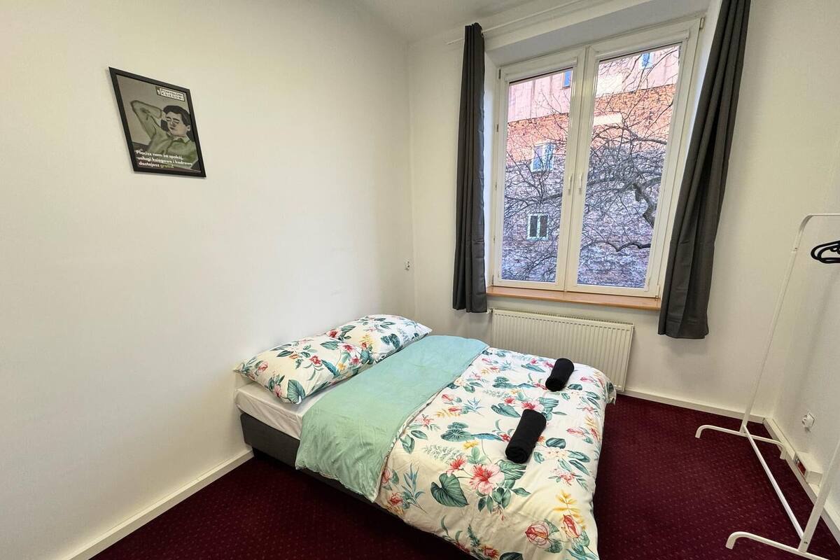 A small, simple room with a bed, a radiator, and a window with curtains.