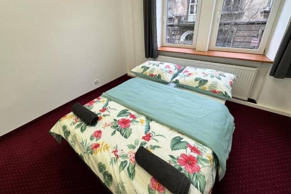 A bedroom with a bed, floral bedding, a window with curtains, and a radiator.