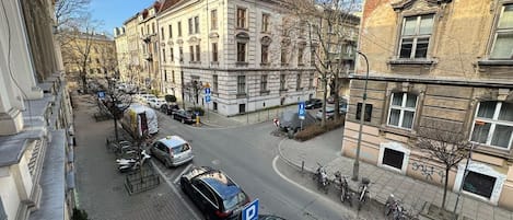 Vista de la calle con automóviles estacionados, un paso de peatones y edificios de arquitectura clásica.