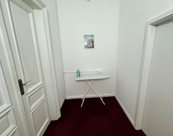 A small room with a white door, a white ironing board, and a small poster on the wall. - Fantastic Inn Kraków - GR6 (Krakow)