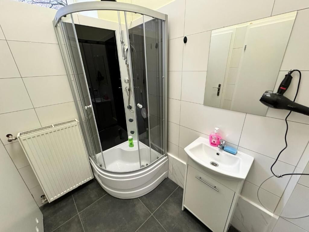 A bathroom with a glass-enclosed shower, a white sink with a mirror, and a radiator.
