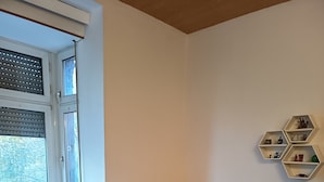 A room with a white desk, black office chair, wooden flooring, a window with blinds, a radiator, and a wall-mounted hexagonal shelf with various items. - 140 sqm, 5 rooms, up to 10 people (Ludwigshafen am Rhein)