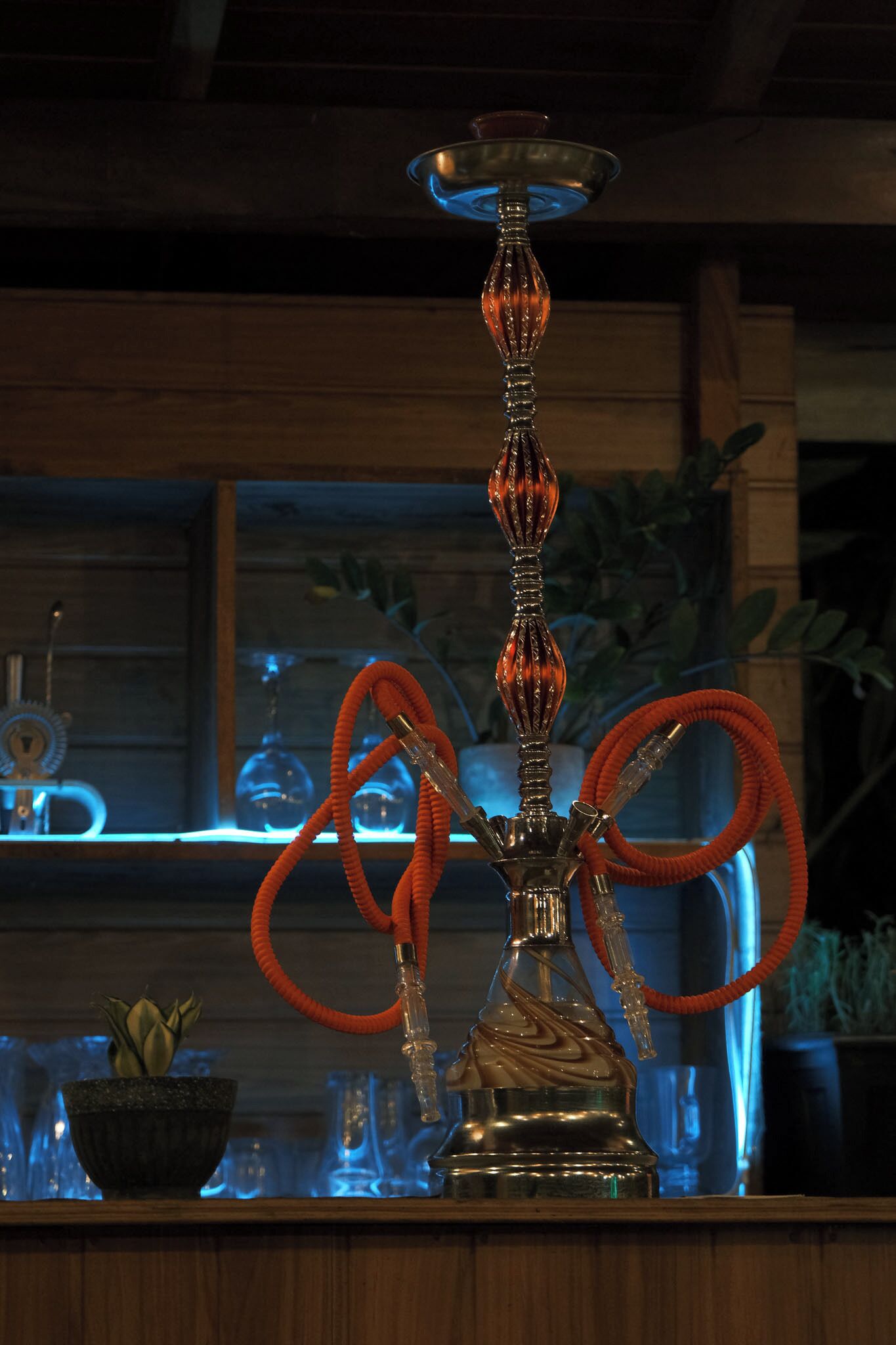 A hookah with a metallic base and a glass chimney, placed on a wooden surface.