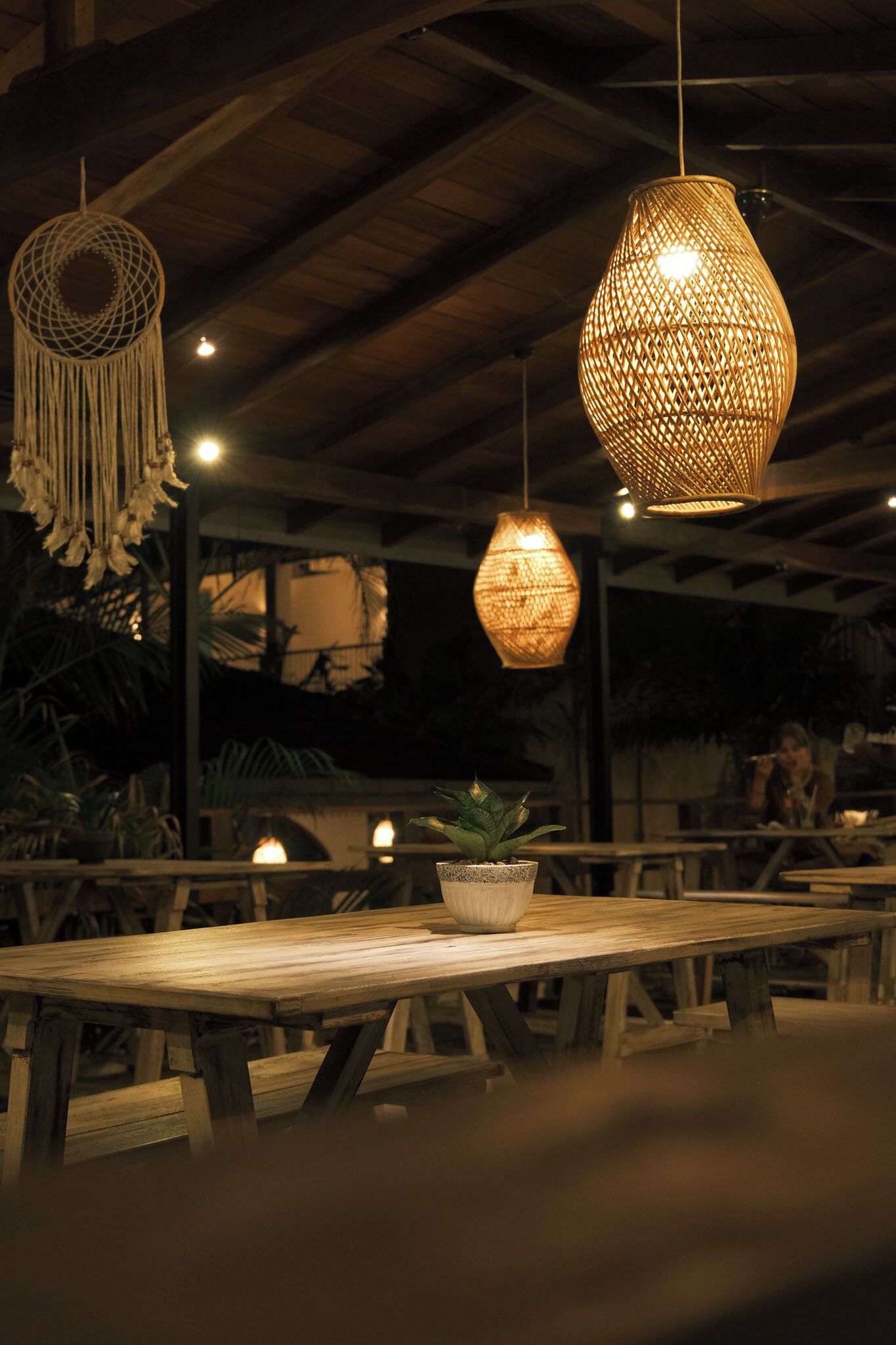A wooden table with a potted plant, surrounded by hanging wicker lamps.