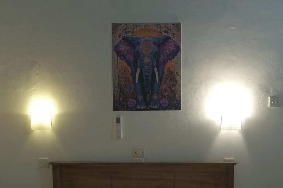 Quarto de hotel com uma cama, duas luzes fixadas na parede, um quadro acima da cama e duas toalhas dispostas em formato de coração sobre a cama.