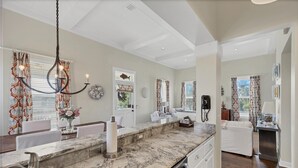 A modern kitchen with marble countertops, a built-in dishwasher, and a dining area with a white table and chairs. - The perfect Beach Cottage getaway! (Placida)