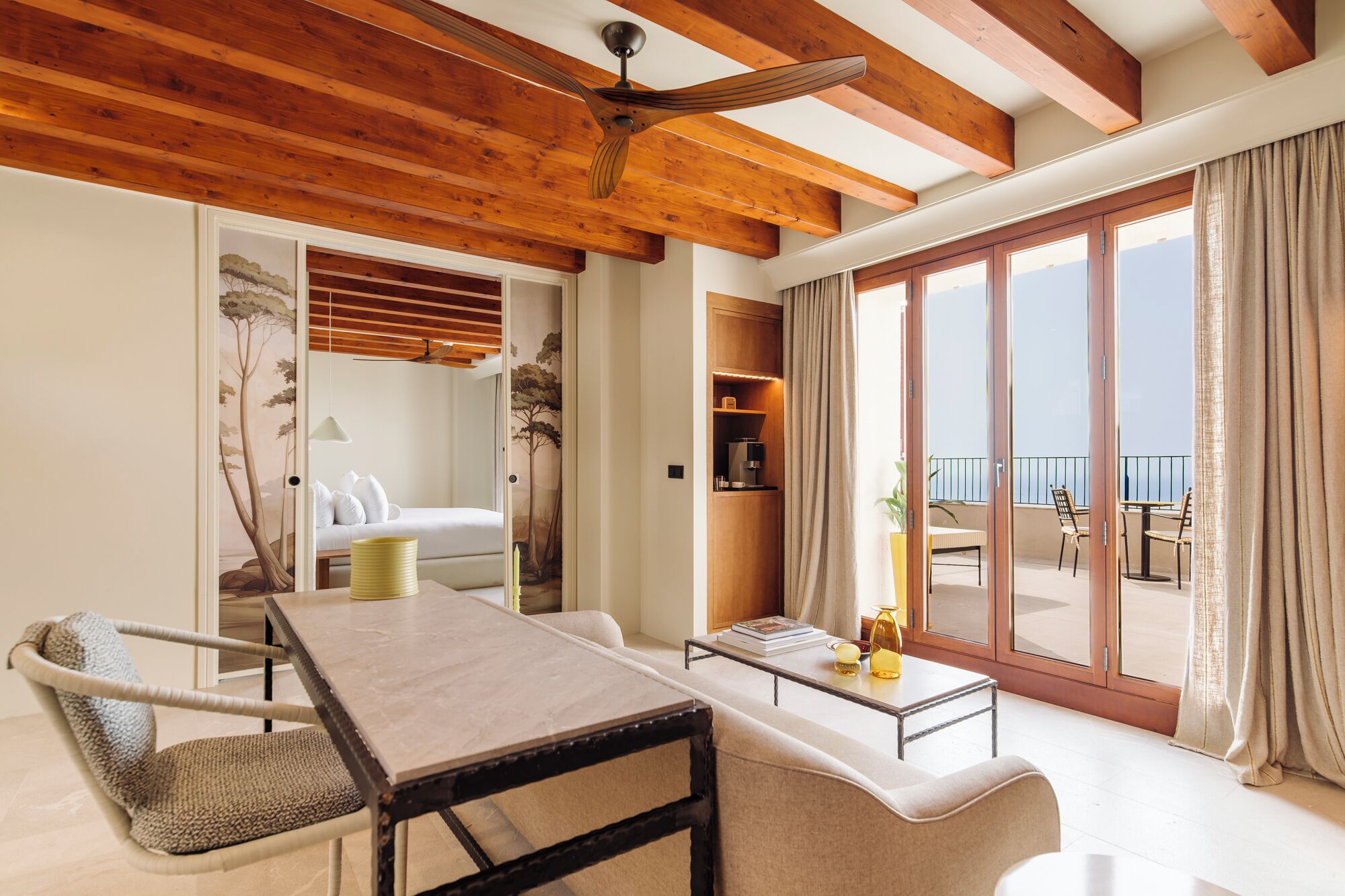 Una habitación con cama, una mesa de comedor, un sofá, una mesa de centro y vistas al mar a través de amplios ventanales correderas.