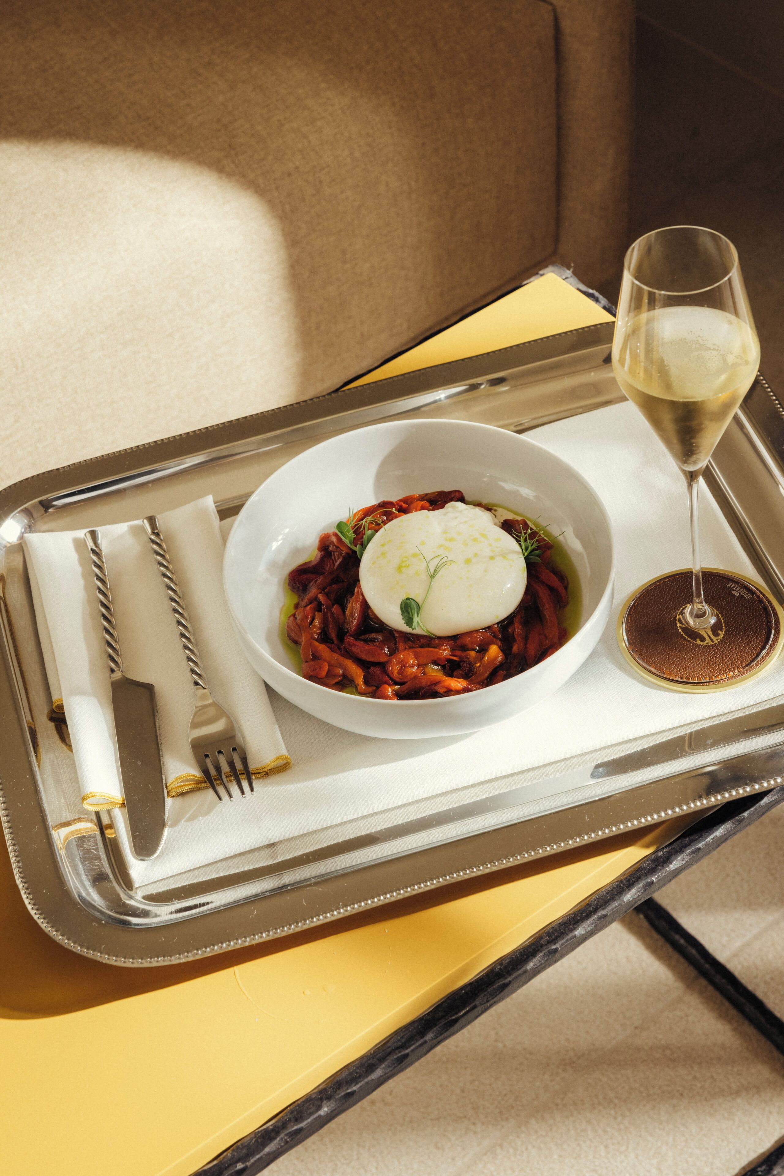 A tray with a plate of food, a glass of white wine, and cutlery on a table.