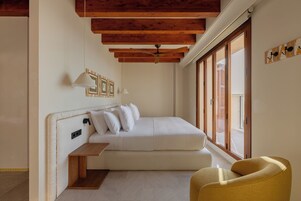 Un dormitorio con cama, mesita de noche, una silla, ventilador de techo y un ventanal grande.