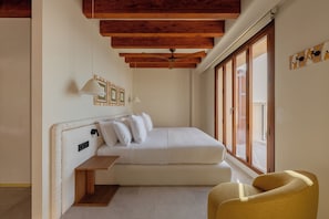 A bedroom with a bed, a bedside table, a chair, a ceiling fan, and a large window. - Gran Hotel Margalida Mallorca by Annua Signature - New Opening (Banyalbufar)