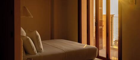 A bedroom with a bed, a bedside table, and a view through a sliding door to an outdoor balcony.