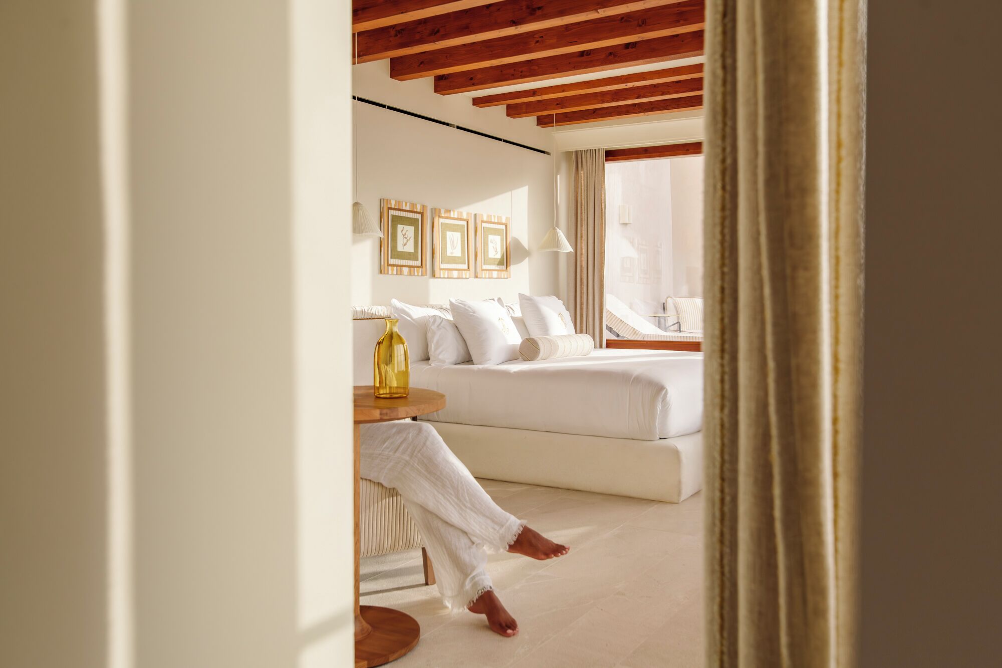 A hotel room with a bed, a round wooden table, and a window with curtains.