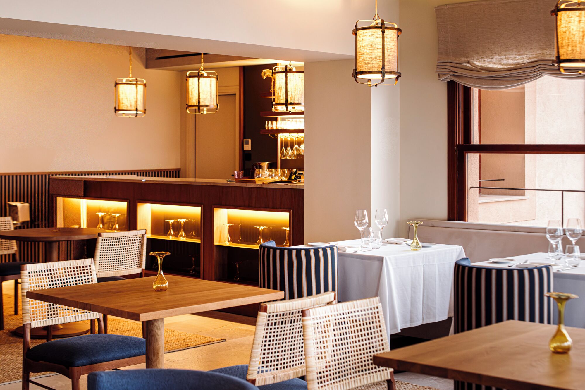 A restaurant interior with wooden tables, wicker chairs, and hanging pendant lights.