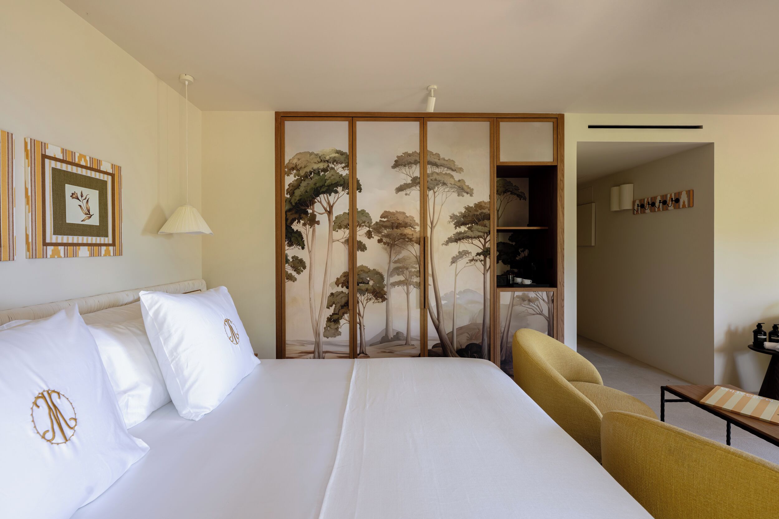 A hotel room with a large bed, a wooden cabinet, a chair, and a wall with framed artwork.