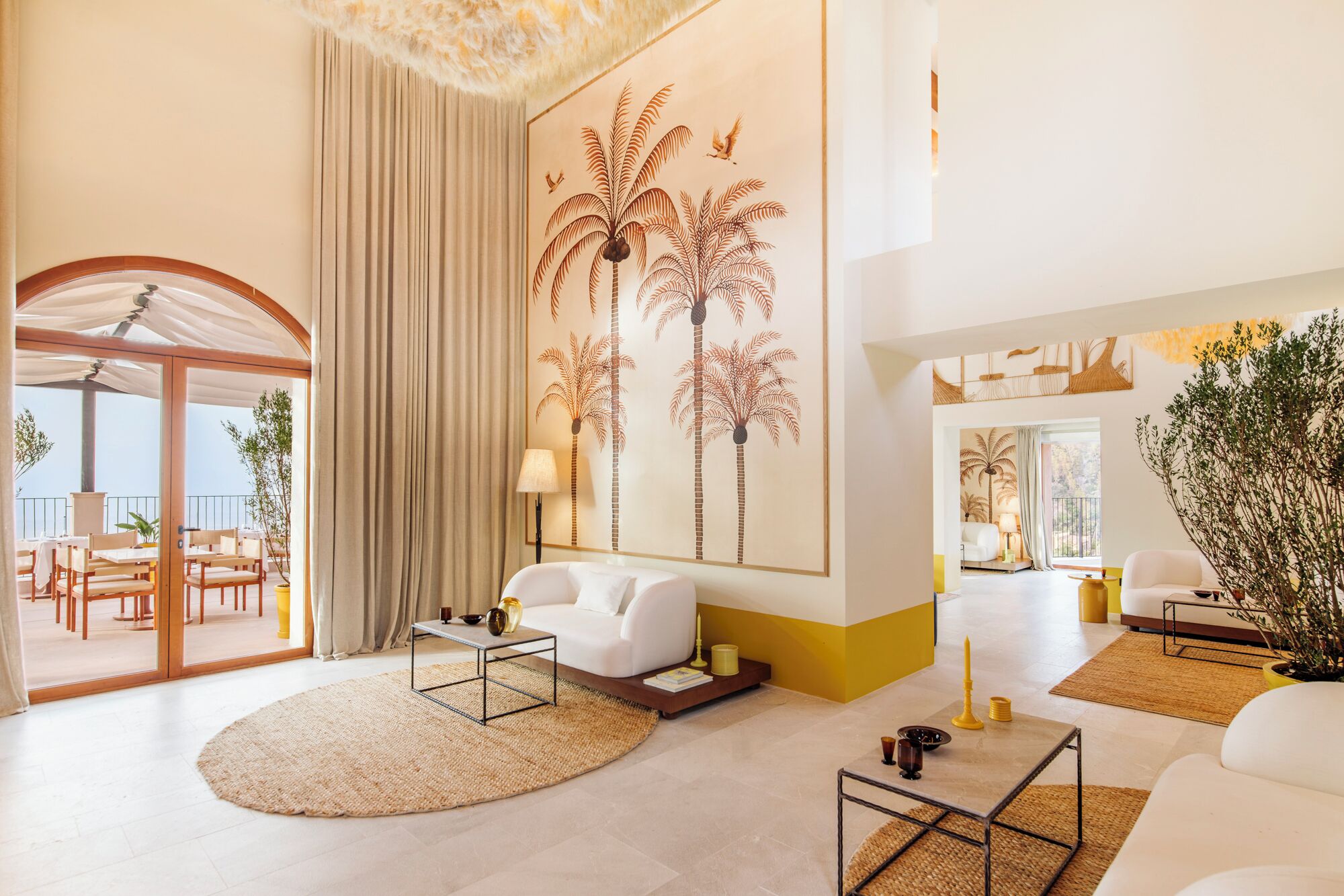 Amplia sala de estar con un gran ventanal, un sofá, una mesa de centro y un muro decorativo con palmeras.