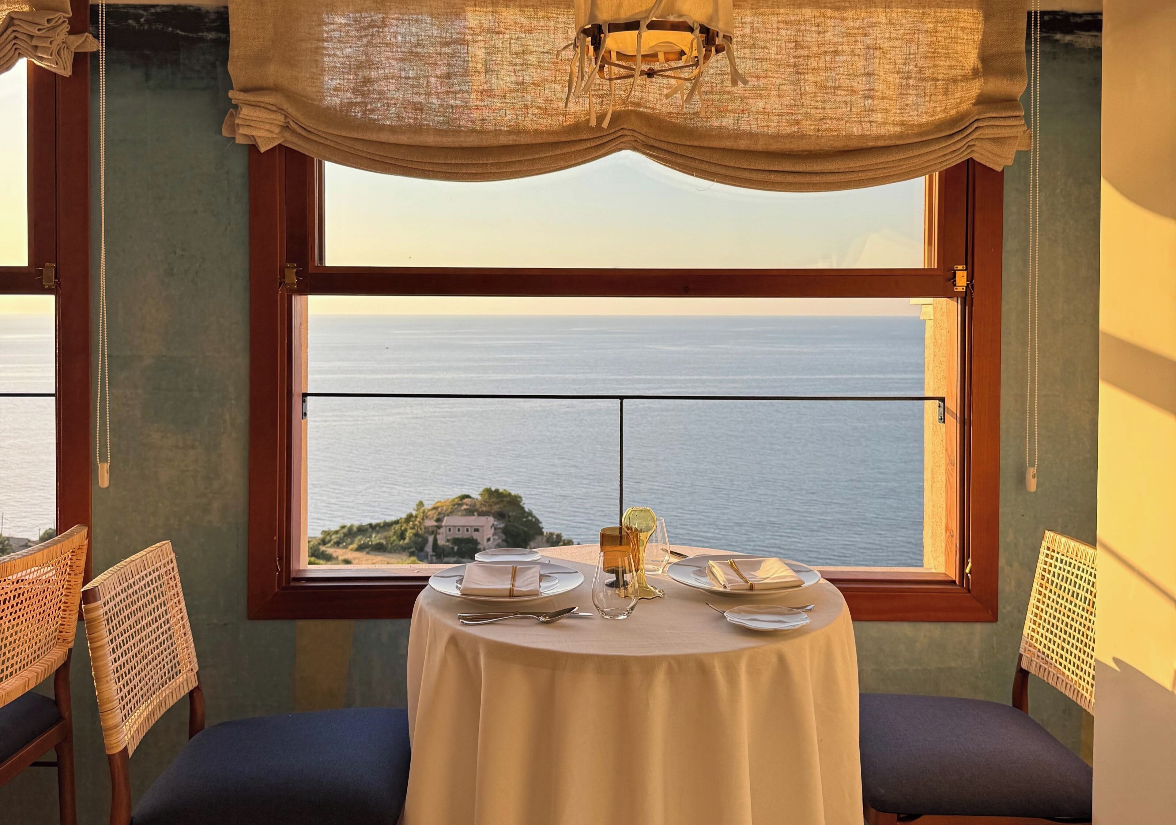 Mesa para dos con vista al mar a través de un ventanal grande.