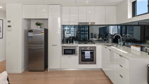 A modern kitchen with white cabinetry, stainless steel appliances, and a large window providing a view of the city. - Central 2BR Gem | Modern Comfort City & River View (Brisbane)