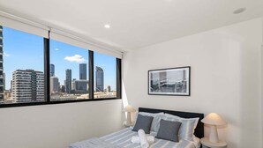 A bedroom with a large bed, two bedside tables, a city view, and a framed picture on the wall. - Central 2BR Gem | Modern Comfort City & River View (Brisbane)