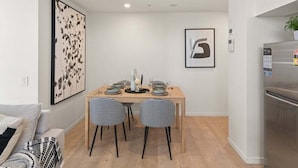 A modern kitchen with a dining table set for four, two checkered chairs, a refrigerator, and a wall-mounted artwork. - Central 2BR Gem | Modern Comfort City & River View (Brisbane)