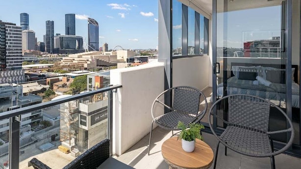 A balcony with two wicker chairs, a small table with a plant, and a city view. - Central 2BR Gem | Modern Comfort City & River View (Brisbane)