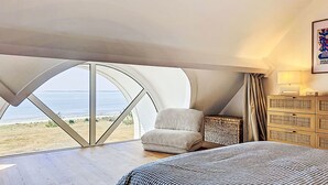 Een slaapkamer met een groot raam, een bed, een stoel en een nachtkastje.