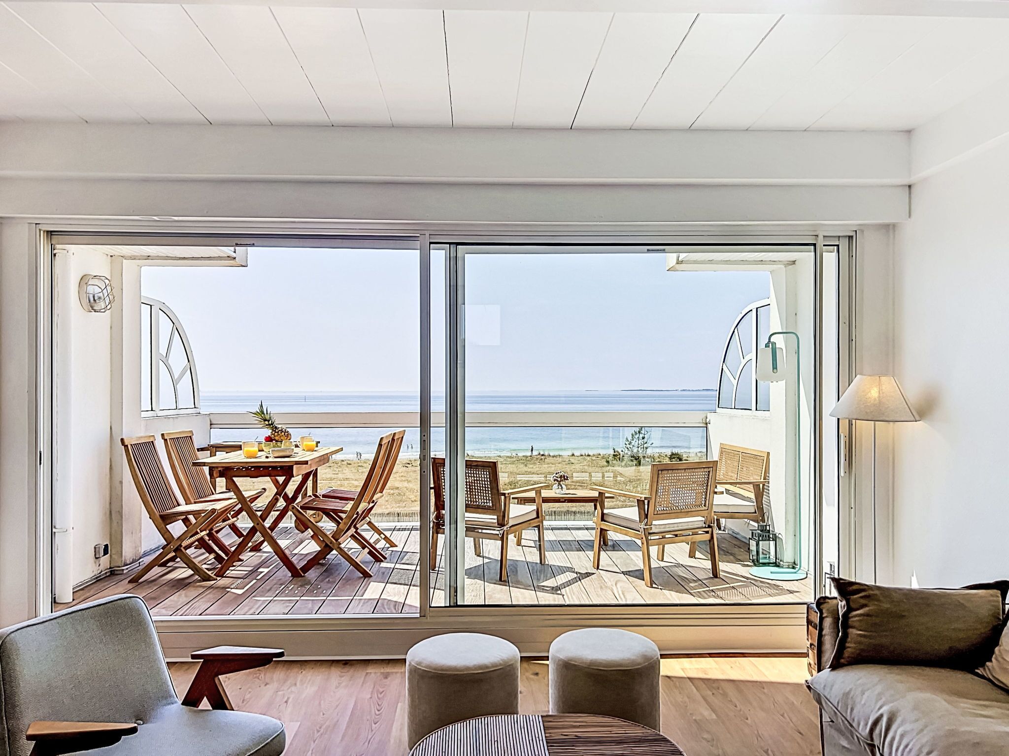 Ein Zimmer mit einer großen Schiebeglastür, die auf eine Terrasse mit Sitzgelegenheiten und Blick auf den Strand führt.