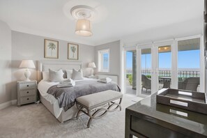 A bedroom with a bed, bedside tables, a bench, a desk, and a balcony with outdoor furniture. - Beautiful Luxury Beach House 4 bed 4 Bath newly renovated (Gorleston-on-Sea)