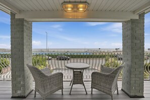 A covered outdoor seating area with wicker chairs and a table, overlooking a beach and a road with parked cars. - Beautiful Luxury Beach House 4 bed 4 Bath newly renovated (Gorleston-on-Sea)