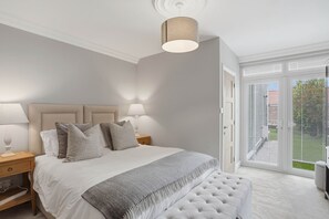 Ein Schlafzimmer mit Bett, Nachttischen, einer Bank, einer Deckenleuchte und einer Glasschiebetür nach draußen.