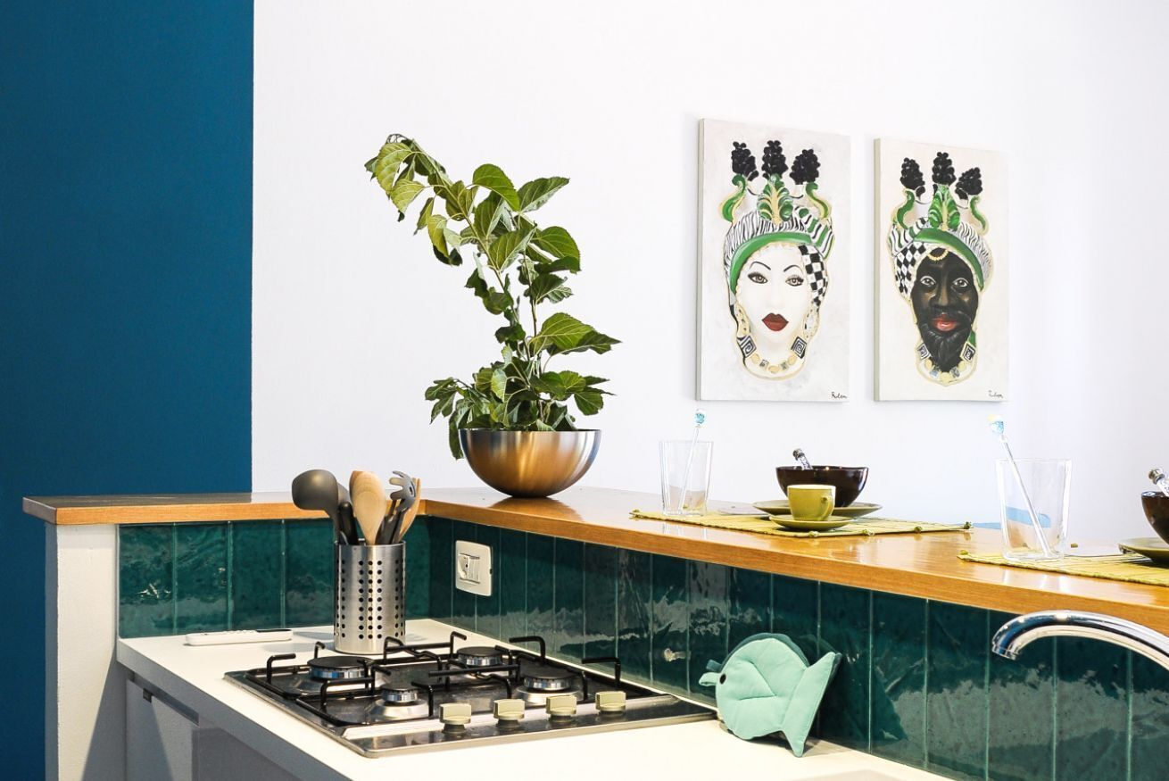 Une cuisine équipée d’une cuisinière à gaz, d’un évier, d’une plante en pot et de deux œuvres d’art accrochées au mur.