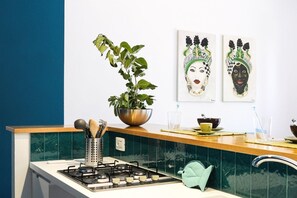 A kitchen with a gas stove, a sink, a potted plant, and two artworks on the wall. - Villa Bruca is a two-family house composed of two separate units.The unit offered, Villa Bruca 1, includes a double bedroom with the possibility of adding two single beds, a spacious bathroom with a modern walk-in shower, and a kitchen-living area equipp (Caronia)
