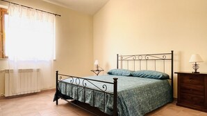 A bedroom with a metal bed frame, a green bedspread, a small bedside table with a lamp, and a wooden dresser. - Villa Bruca is a two-family house composed of two separate units.The unit offered, Villa Bruca 1, includes a double bedroom with the possibility of adding two single beds, a spacious bathroom with a modern walk-in shower, and a kitchen-living area equipp (Caronia)