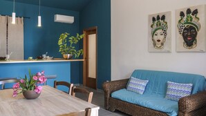 Un comedor con una mesa y sillas de madera, un sofá azul y una pared con dos máscaras decorativas.