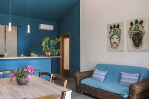 A dining area with a wooden table and chairs, a blue sofa, and a wall with two decorative masks. - Villa Bruca is a two-family house composed of two separate units.The unit offered, Villa Bruca 1, includes a double bedroom with the possibility of adding two single beds, a spacious bathroom with a modern walk-in shower, and a kitchen-living area equipp (Caronia)