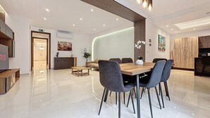 Een moderne eethoek met een houten tafel en stoelen, een televisie en een keuken op de achtergrond.