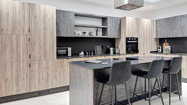 Een moderne keuken met een centraal eiland, barstoelen, inbouwapparatuur en houten kastjes.