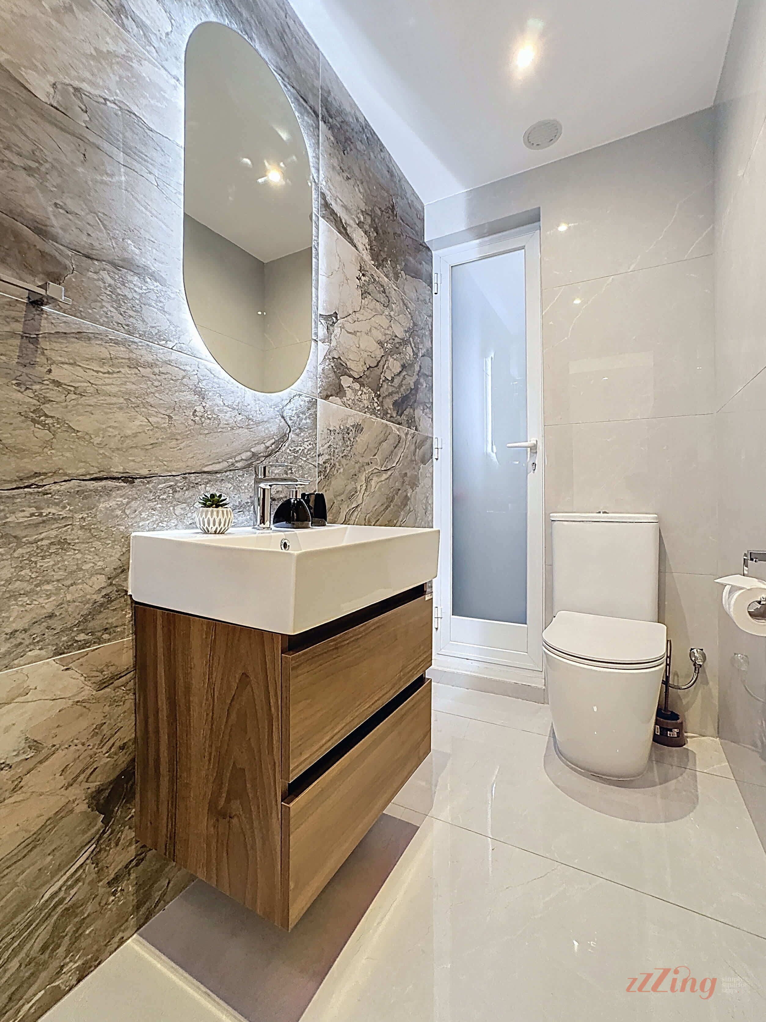 A modern bathroom with a marble wall, a wooden vanity, a toilet, and a mirror.