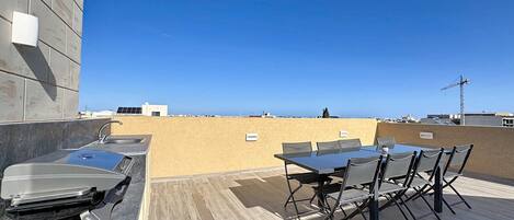 Una terraza en la azotea con mesa, sillas, un lavamanos y vistas del horizonte de la ciudad.