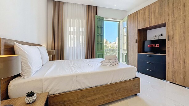 A modern bedroom with a large bed, a TV, and a wooden wardrobe. - Rooftop Villa w/ Pvt Plunge Pool & BBQ in South (Ħal Għaxaq)