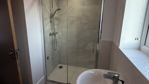 A modern bathroom with a glass-enclosed shower, a white sink, and a window providing natural light. - Modern 3-Bedroom Home in Bletchley, Milton Keynes (Bletchley)