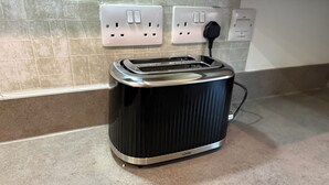 A black toaster on a kitchen countertop with a tiled backsplash and electrical outlets. - Modern 3-Bedroom Home in Bletchley, Milton Keynes (Bletchley)