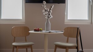 A dining area with a round table, two chairs, a vase with flowers, and a television mounted on the wall. - Hotel Zest Den Haag - Scheveningen (The Hague)