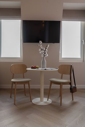A dining area with a round table, two chairs, a vase with flowers, and a television mounted on the wall. - Hotel Zest Den Haag - Scheveningen (The Hague)