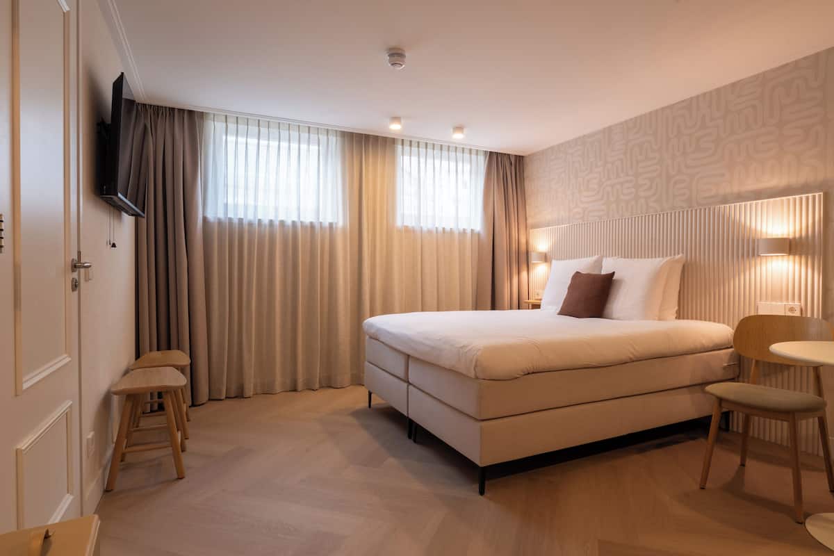 Quarto de hotel com cama, televisão, escrivaninha e cadeira.
