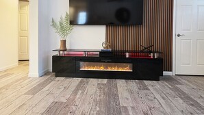 Un salon moderne avec un téléviseur à écran plat fixé à un mur en bois, un meuble de rangement noir intégrant une cheminée et une plante en pot.